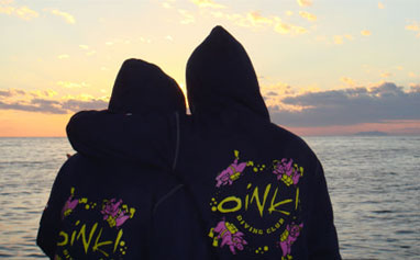Due ragazzi dell'Oink Diving, di spalle, ammirano uno splendido tramonto